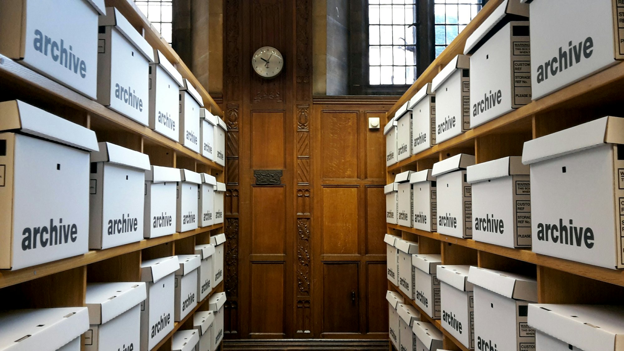 Rows of white archive boxes on wooden shelves leading to a panelled door