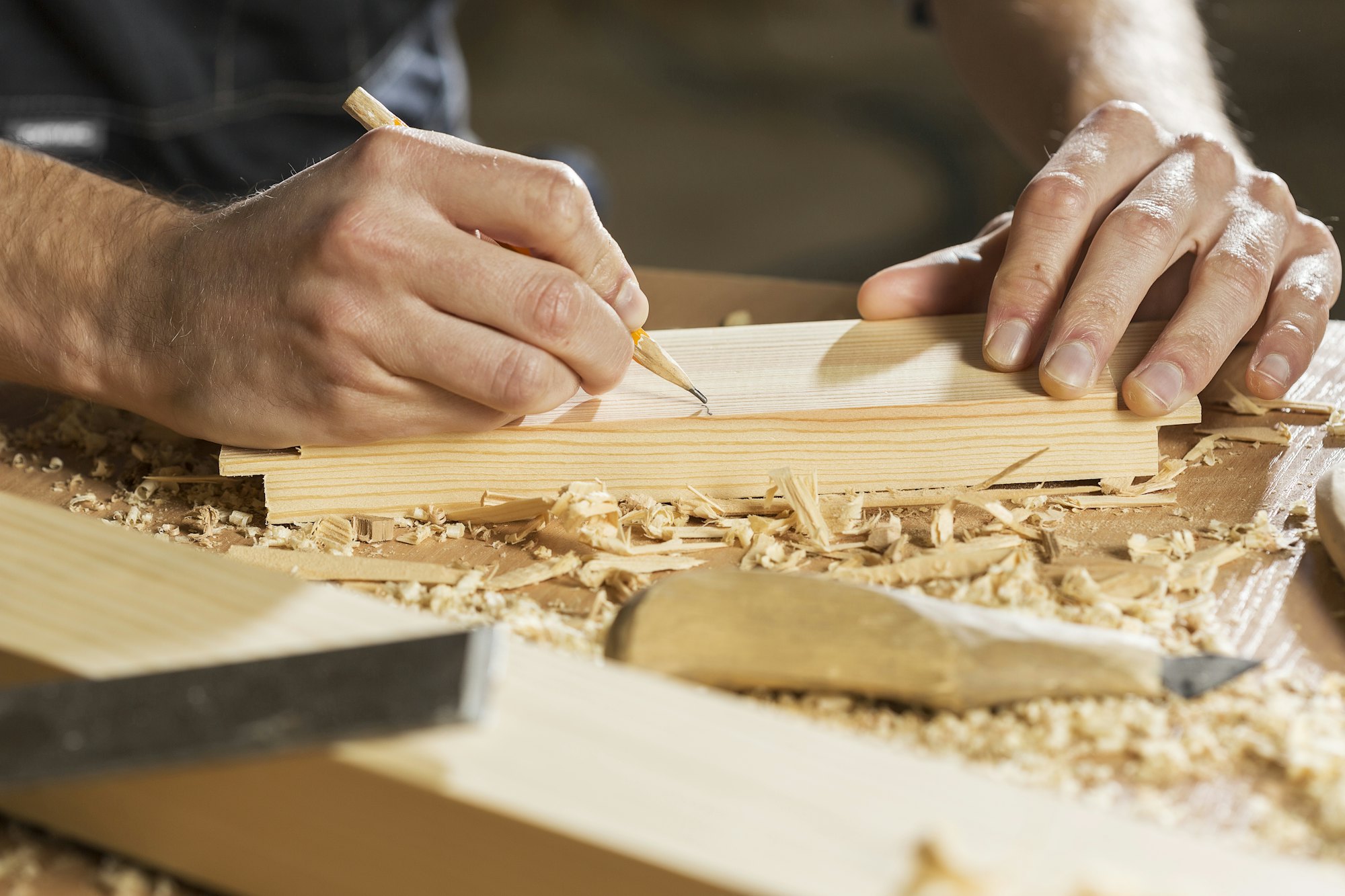 Hands marking a line with a pencil on a wooden board among wood shavings