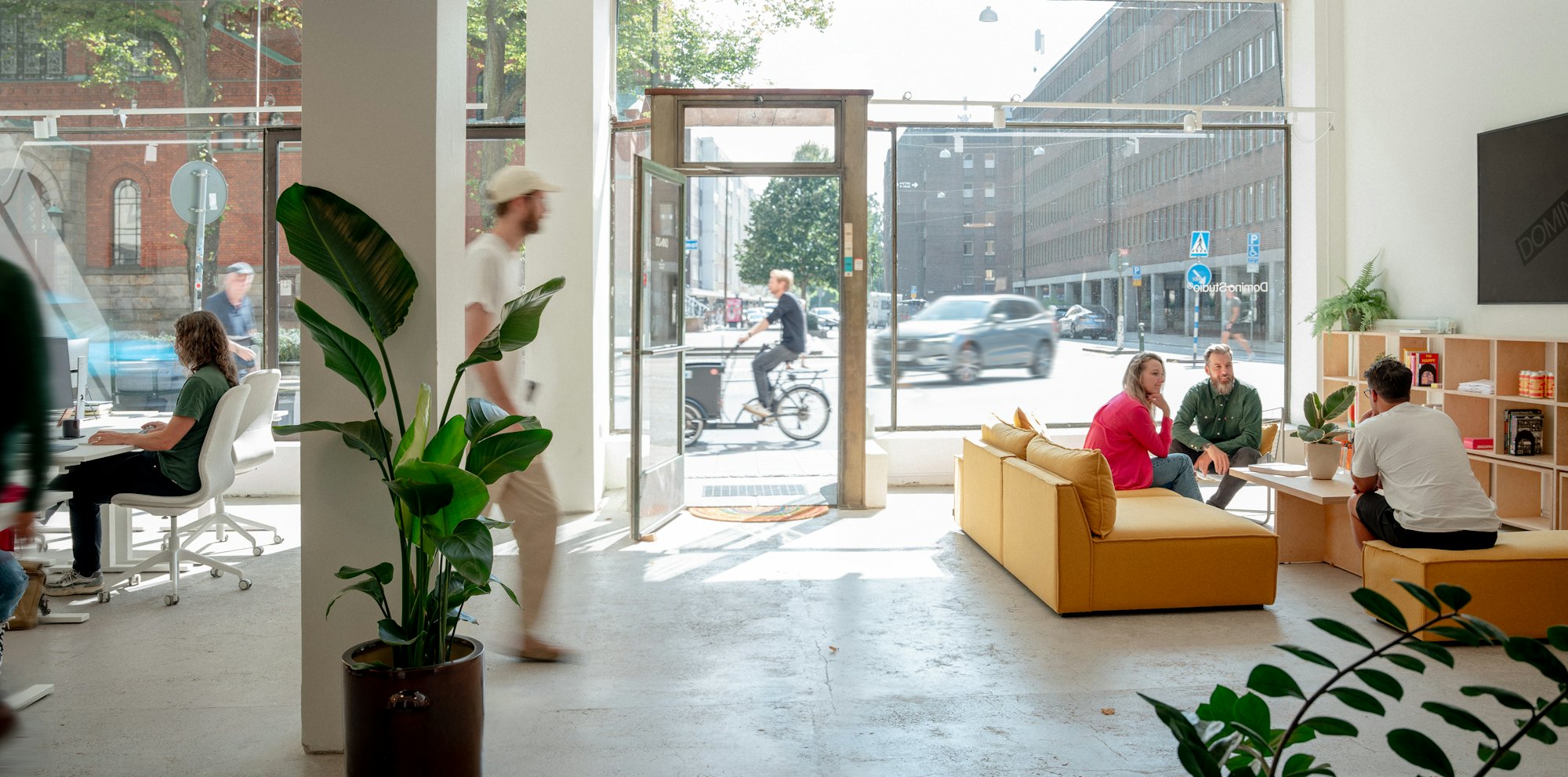 Small studio on a ground floor with people working at desks and talking on a sofa by street-facing windows
