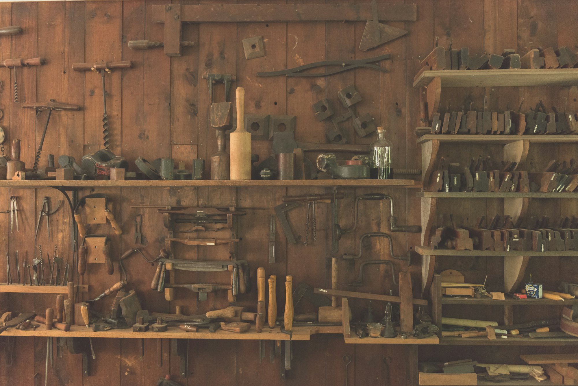 Workshop wall of old hand tools hung on wooden shelves